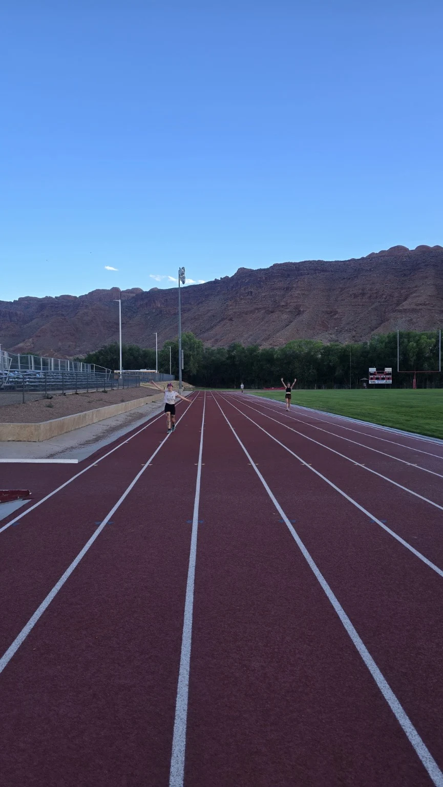 Runners on the high school track with red cliffs behind them